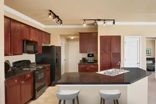 kitchen featuring a breakfast bar area, refrigerator, electric range oven, microwave, light floors, dark granite-like countertops, and brown cabinetry