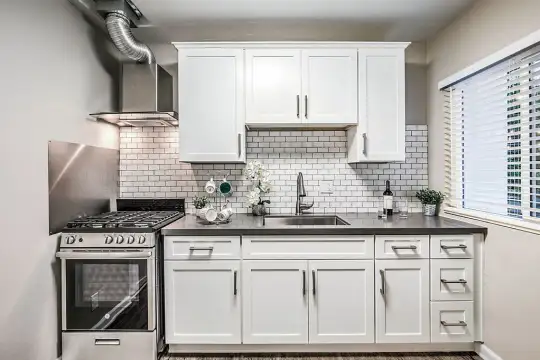 kitchen with natural light, gas range oven, range hood, stainless steel finishes, white cabinets, dark countertops, and dark floors