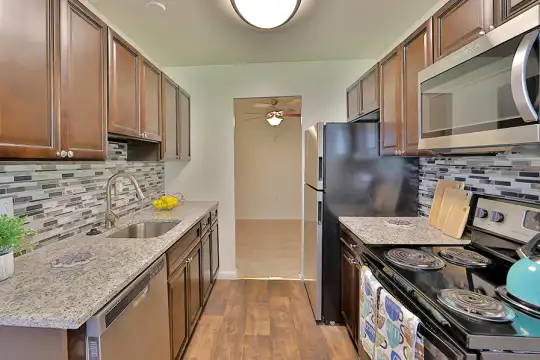 kitchen with electric range oven, dishwasher, stainless steel microwave, brown cabinets, pendant lighting, light granite-like countertops, and light hardwood floors