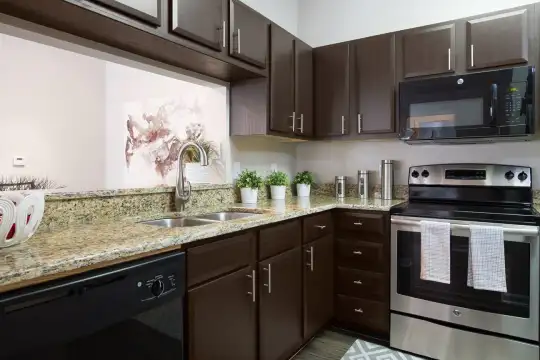 kitchen with dishwasher, electric range oven, microwave, light floors, light stone countertops, and dark brown cabinetry