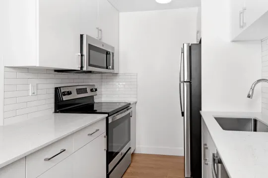 kitchen featuring stainless steel appliances, electric range oven, white cabinetry, light parquet floors, and light granite-like countertops