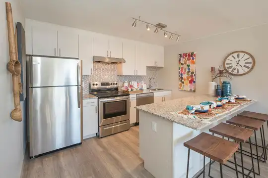 kitchen featuring a kitchen bar, ventilation hood, electric range oven, stainless steel refrigerator, dishwasher, light hardwood floors, white cabinetry, and light stone countertops