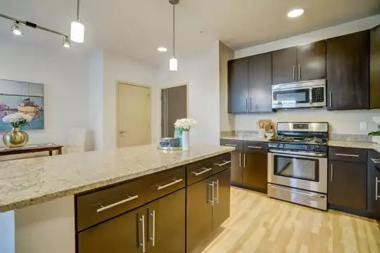 kitchen with gas range oven, stainless steel microwave, pendant lighting, light parquet floors, dark brown cabinets, and light stone countertops