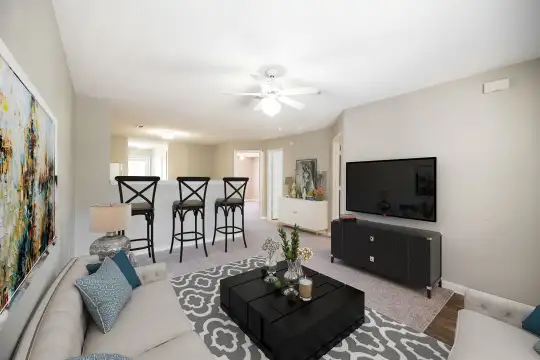 carpeted living room with a ceiling fan, a kitchen breakfast bar, and TV