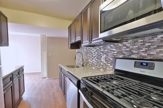 kitchen featuring refrigerator, stainless steel microwave, dishwasher, gas stovetop, dark brown cabinets, light stone countertops, and light hardwood floors