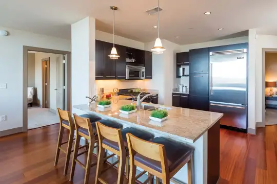 kitchen with a kitchen island, a breakfast bar area, stainless steel refrigerator, range oven, microwave, dark parquet floors, pendant lighting, dark brown cabinetry, and light granite-like countertops