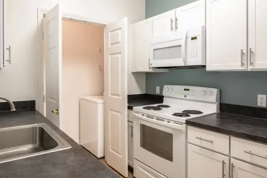 kitchen featuring washer / dryer, electric range oven, microwave, dark countertops, light floors, and white cabinetry