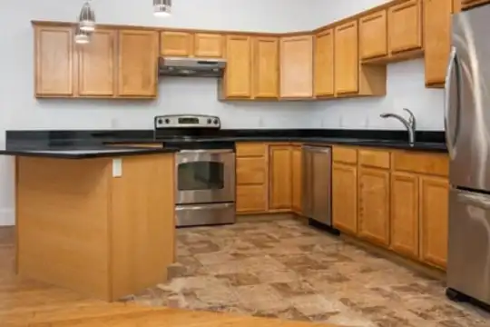 kitchen featuring stainless steel appliances, range oven, exhaust hood, dark countertops, pendant lighting, brown cabinets, and dark floors