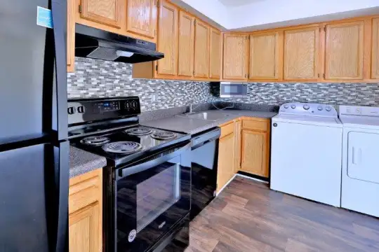 kitchen featuring independent washer and dryer, dishwasher, electric range oven, refrigerator, exhaust hood, dark parquet floors, dark stone countertops, and brown cabinetry