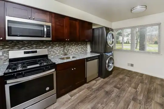 kitchen with natural light, dishwasher, gas range oven, independent washer and dryer, stainless steel microwave, dark brown cabinets, light hardwood floors, and light stone countertops
