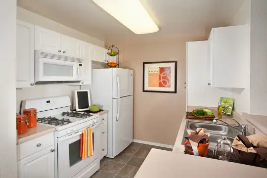 kitchen featuring gas range oven, refrigerator, microwave, light countertops, dark tile floors, and white cabinetry