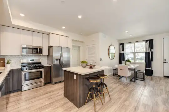 kitchen featuring natural light, a breakfast bar area, stainless steel appliances, gas range oven, white cabinetry, light hardwood floors, and light countertops