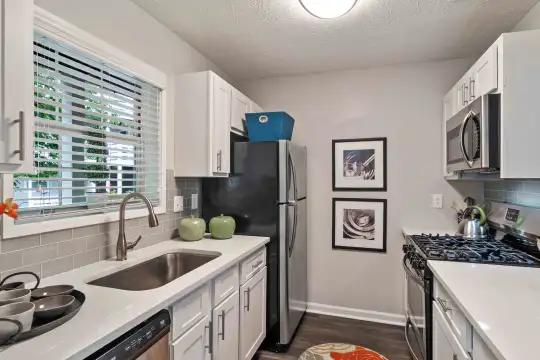 kitchen with natural light, stainless steel microwave, gas range oven, dishwasher, refrigerator, light countertops, white cabinetry, and dark hardwood floors