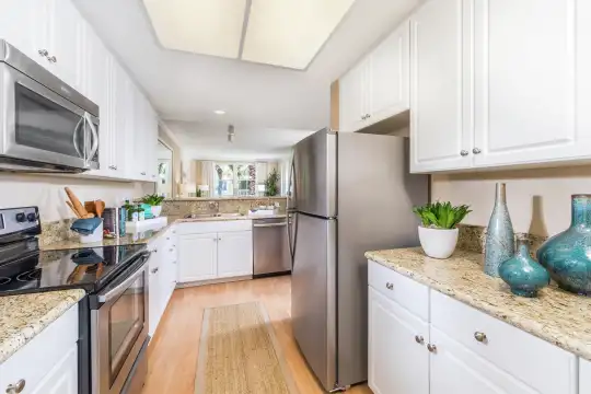 kitchen featuring electric range oven, refrigerator, dishwasher, stainless steel microwave, white cabinetry, light stone countertops, and light parquet floors