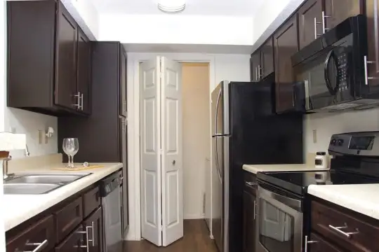 kitchen with refrigerator, electric range oven, dishwasher, microwave, dark brown cabinetry, light countertops, and dark hardwood flooring