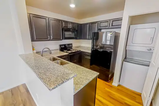 kitchen featuring washer / dryer, refrigerator, electric range oven, microwave, light stone countertops, light parquet floors, and dark brown cabinets