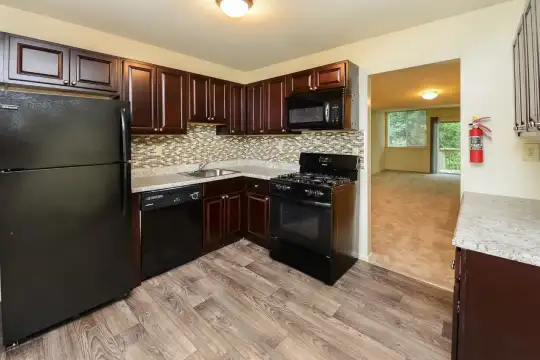 kitchen with gas range oven, refrigerator, dishwasher, microwave, dark brown cabinets, light stone countertops, and light parquet floors