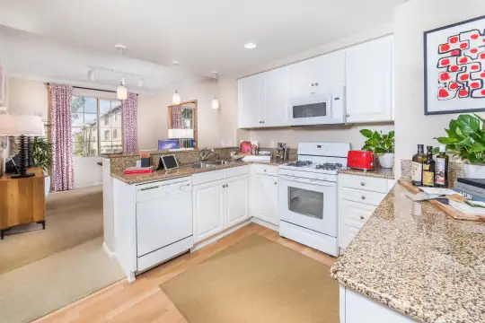 kitchen featuring natural light, gas range oven, dishwasher, microwave, stone countertops, white cabinetry, pendant lighting, and light hardwood flooring