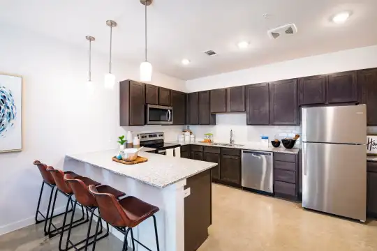 kitchen featuring a kitchen bar, stainless steel appliances, range oven, dark brown cabinetry, light granite-like countertops, pendant lighting, and light tile floors