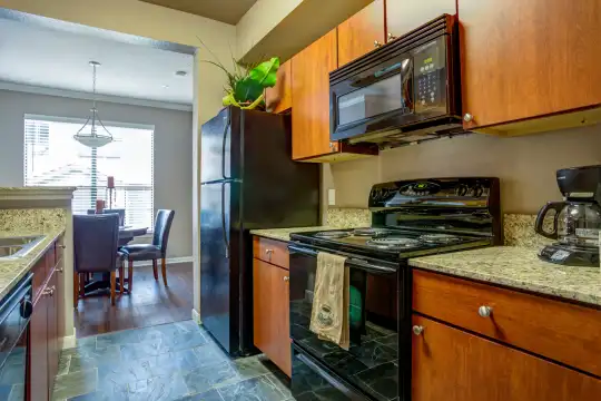 kitchen featuring natural light, refrigerator, dishwasher, electric range oven, microwave, light tile floors, pendant lighting, light granite-like countertops, and brown cabinets