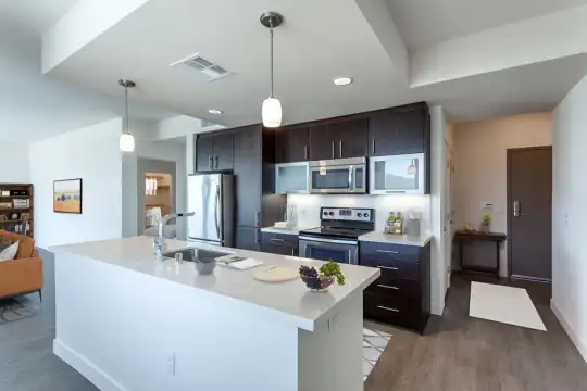 kitchen featuring stainless steel appliances, electric range oven, a kitchen island with sink, light countertops, dark parquet floors, pendant lighting, and white cabinets