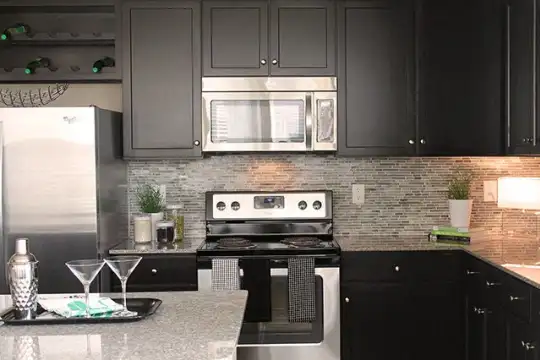 kitchen featuring refrigerator, electric range oven, stainless steel microwave, light stone countertops, and dark brown cabinets