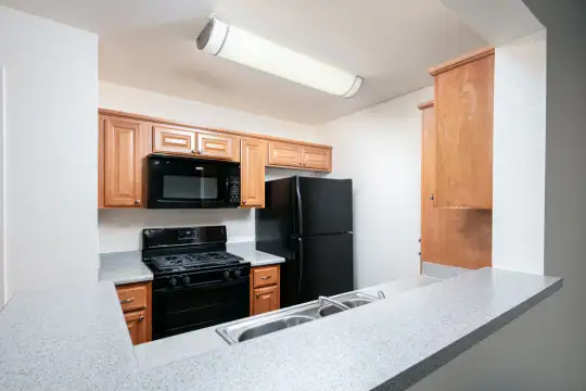 kitchen featuring gas range oven, refrigerator, microwave, light granite-like countertops, and brown cabinets