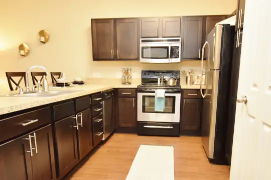 kitchen featuring refrigerator, electric range oven, stainless steel microwave, light stone countertops, light parquet floors, and dark brown cabinetry