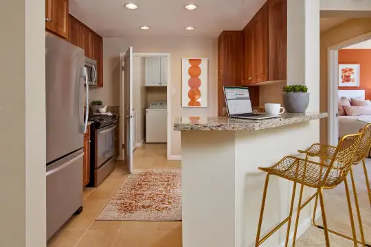 kitchen featuring a kitchen bar, washer / dryer, stainless steel refrigerator, range oven, microwave, granite-like countertops, light tile flooring, and brown cabinetry