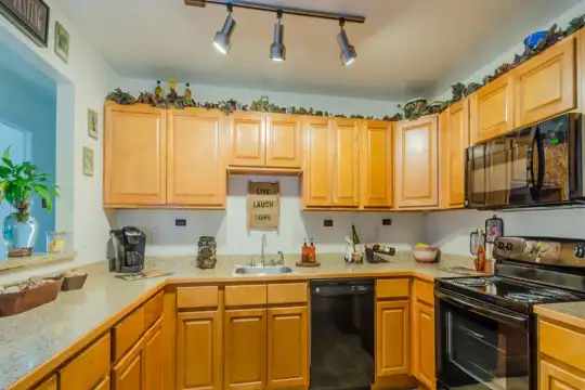 kitchen with electric range oven, dishwasher, microwave, light tile floors, brown cabinets, and light countertops
