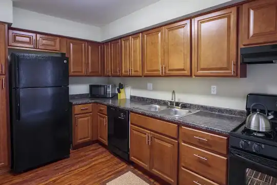 kitchen with range hood, refrigerator, microwave, dishwasher, gas range oven, dark hardwood flooring, dark granite-like countertops, and brown cabinetry
