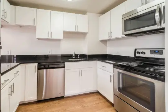 kitchen with stainless steel appliances, electric range oven, dark countertops, white cabinets, and light hardwood floors