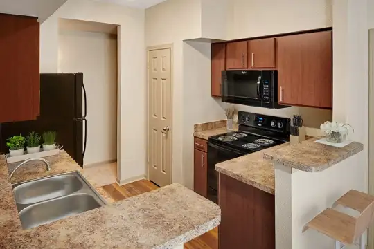 kitchen with refrigerator, electric range oven, microwave, stone countertops, light floors, and brown cabinets
