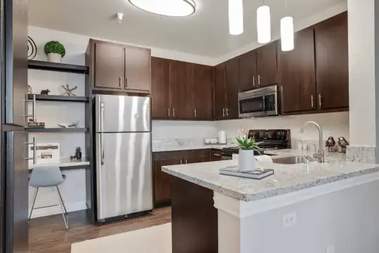 kitchen featuring stainless steel appliances, range oven, dark hardwood floors, pendant lighting, dark brown cabinets, and light stone countertops
