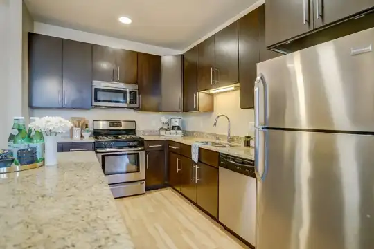 kitchen featuring gas range oven, stainless steel appliances, light hardwood floors, dark brown cabinets, and light granite-like countertops