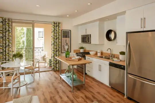 kitchen featuring natural light, beamed ceiling, stainless steel appliances, gas range oven, white cabinetry, light parquet floors, and light countertops