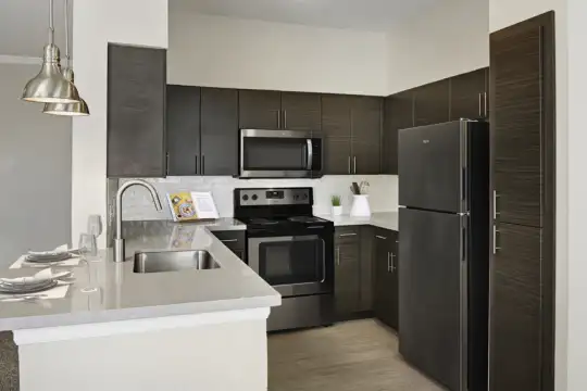 kitchen featuring refrigerator, electric range oven, stainless steel microwave, pendant lighting, dark brown cabinetry, light countertops, and light flooring