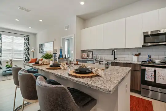 kitchen with a center island, natural light, range oven, stainless steel microwave, white cabinetry, light flooring, and light granite-like countertops