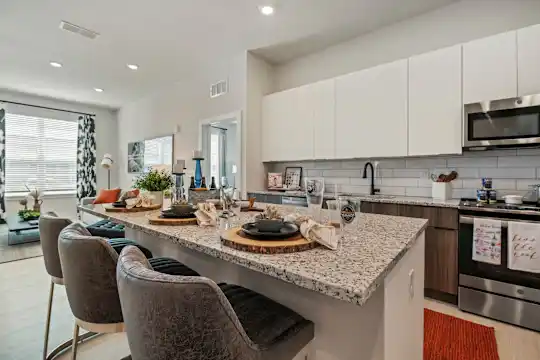 kitchen with a center island, natural light, range oven, stainless steel microwave, white cabinetry, light flooring, and light granite-like countertops