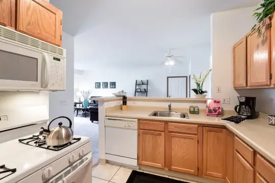 kitchen featuring dishwasher, microwave, light countertops, light tile flooring, and brown cabinets