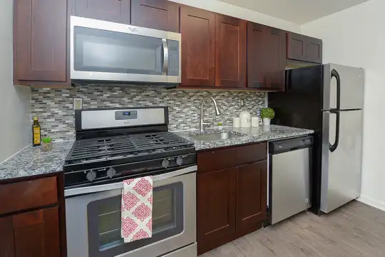 kitchen featuring refrigerator, gas range oven, dishwasher, stainless steel microwave, light parquet floors, light granite-like countertops, and dark brown cabinets