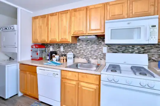 kitchen with washer / dryer, gas range oven, dishwasher, microwave, dark flooring, light countertops, and brown cabinets