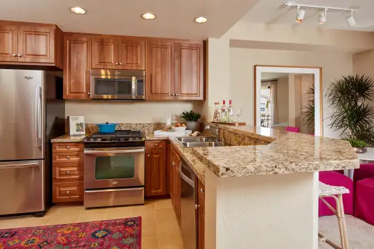 kitchen with stainless steel appliances, range oven, light tile floors, stone countertops, and brown cabinets