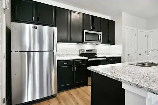 kitchen featuring a center island, stainless steel appliances, electric range oven, pendant lighting, light hardwood flooring, light stone countertops, and dark brown cabinetry