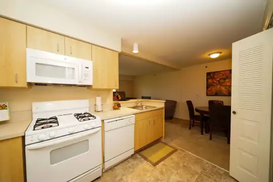 kitchen with gas range oven, dishwasher, microwave, light tile floors, light brown cabinets, and light countertops