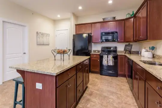 kitchen featuring a kitchen island, a kitchen breakfast bar, range oven, refrigerator, dishwasher, microwave, light tile floors, stone countertops, and brown cabinetry