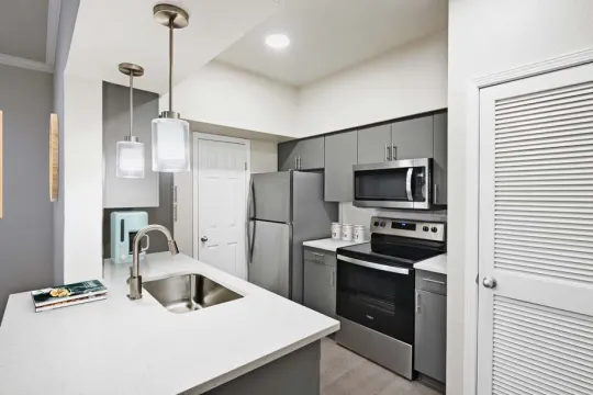 kitchen featuring stainless steel appliances, electric range oven, a kitchen island with sink, light countertops, light parquet floors, pendant lighting, and white cabinets