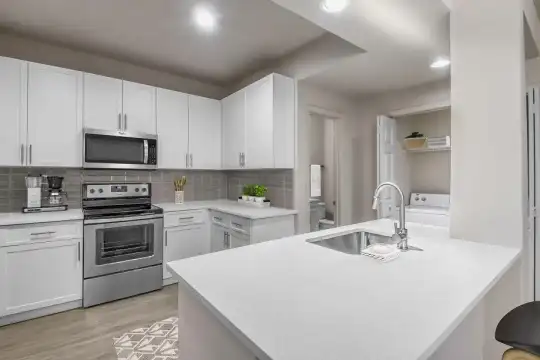 kitchen featuring stainless steel microwave, electric range oven, light countertops, white cabinetry, an island with sink, and light hardwood flooring