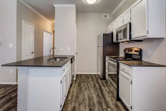 kitchen with stainless steel microwave, refrigerator, electric range oven, dishwasher, pendant lighting, dark countertops, white cabinetry, an island with sink, and dark hardwood floors