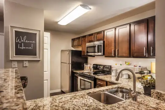 kitchen with refrigerator, electric range oven, stainless steel microwave, light stone countertops, and dark brown cabinetry
